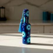 A hand pouring cold water into a glass of elenianna ouzo over ice, showing the liquid transforming into a milky white color.