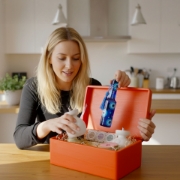 Close-up of a hand placing a bottle of LADOLEA organic extra virgin olive oil inside a red wooden gift crate, highlighting the premium contents.