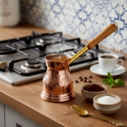 Preparing traditional Greek coffee in a steaming copper briki on a gas stove.