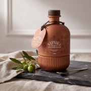 A bottle of Nafsika Premium Extra Virgin Olive Oil presented on a dark marble slab with fresh green olives on a branch and a linen cloth.